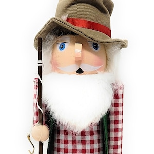 May include: A wooden nutcracker figurine of a man wearing a brown hat, red and white plaid shirt, and black pants. He is holding a fishing pole and a small bucket. The base of the nutcracker is red with the name "BILLY" written in gold lettering.