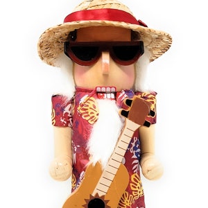 May include: Wooden nutcracker figurine of a man in a Hawaiian shirt, straw hat, and sunglasses, holding a ukulele. The figurine has a white beard, blue shorts, and sandals, standing on a cork base.