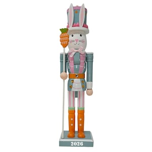 May include: A decorative Easter-themed nutcracker figurine. The figurine is painted in pastel colors, including blue, pink, and orange. It features a bunny head with a top hat and holds a carrot. The base of the figurine has the number "2026".