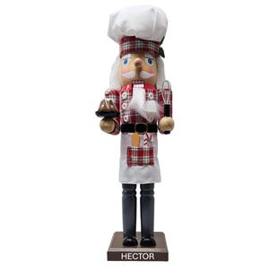 May include: A wooden nutcracker in the shape of a chef, wearing a white chef's hat and a red and white plaid jacket and apron. The nutcracker holds a whisk and a plate with a cake. The base reads "HECTOR".