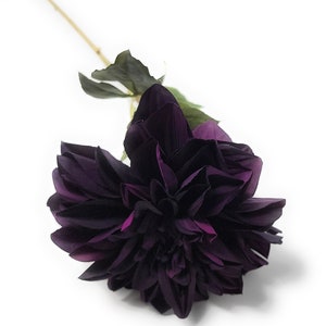 May include: A single dark purple artificial dahlia flower with a stem and leaves.