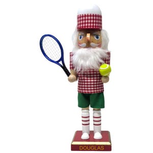 May include: A nutcracker figure wearing a red and white gingham shirt and hat, green shorts, and white socks with red stripes. The figure has a white beard, holds a blue tennis racket in one hand and a yellow tennis ball in the other, standing on a base labeled DOUGLAS.