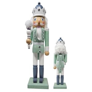 May include: Two decorative nutcrackers, one large and one small, in a seafoam green and white color scheme. The larger nutcracker holds a seashell and wears a crown. The smaller nutcracker has "CAPE COD" printed on its back.