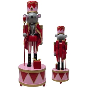 May include: Two mouse nutcracker figurines standing on circular drum bases. The mice wear red and pink uniforms with gold trim, tall hats, and hold staffs. The larger mouse stands next to a red gift box, while the smaller one has 2026 printed on its base.