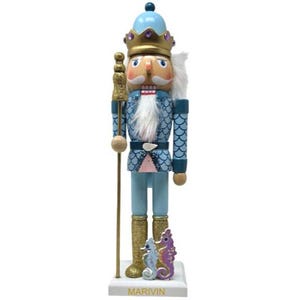 May include: A nutcracker figurine wearing a gold crown and a blue scale-patterned jacket. It has a white beard, holds a gold staff, and stands on a white base labeled MARIVIN. Two small seahorse figures in blue and purple are at its feet.