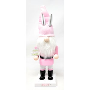 May include: A pink Easter gnome figurine with a white beard, holding a sign that reads "HAPPY EASTER!". The gnome wears a pink hat with silver bunny ears and black boots. The base is white with the name "JOST".