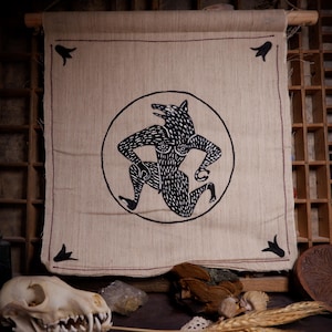 Puede incluir: Un tapiz beige con una ilustración negra de una figura de lobo dentro de un círculo. La figura se representa en una pose de carrera. El tapiz está enmarcado con una barra de madera y tiene detalles negros en las esquinas.