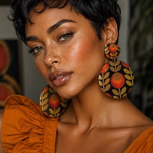 May include: Large circular drop earrings featuring a black background with a repeating floral pattern in shades of orange, red, and gold. The earrings consist of a smaller circular stud connected to a larger circular pendant, both displaying the same motif.