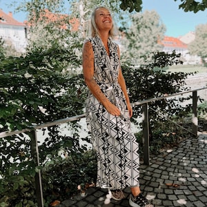 Può includere: Una tuta senza maniche con stampa geometrica in bianco e nero con cintura abbinata. La persona indossa scarpe da ginnastica con stampa leopardata. Lo sfondo comprende vegetazione, una ringhiera metallica e un sentiero acciottolato.