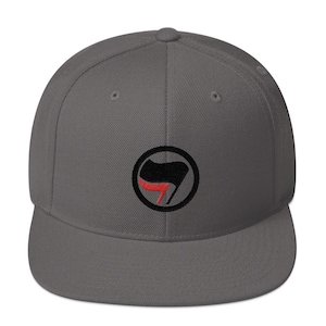 May include: A gray, flat-brimmed baseball cap with a black and red anarchy symbol embroidered on the front.