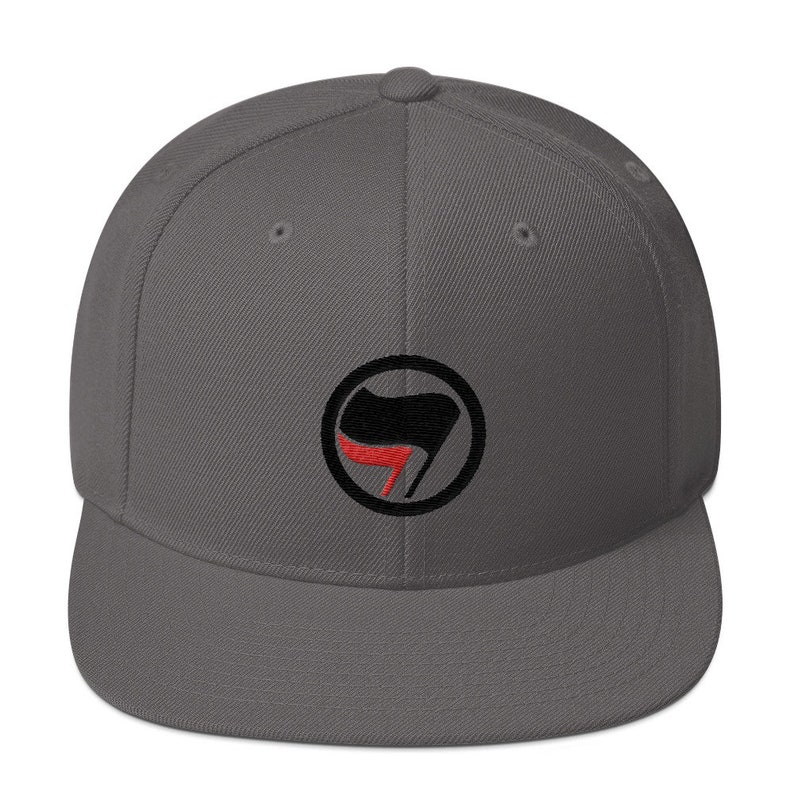 May include: A gray, flat-brimmed baseball cap with a black and red anarchy symbol embroidered on the front.