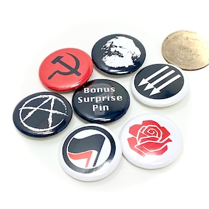 May include: A set of eight 1-inch button pins with various political symbols and slogans. The pins feature a red hammer and sickle, a black anarchy symbol, a black flag with a red diagonal line, a black flag with three white arrows, a red rose, a black and white image of Karl Marx, and a black button with the text "Bonus Surprise Pin".