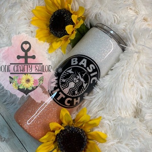 May include: A white and peach glitter tumbler with a black and white graphic of a witch with the text "Basic Witch" on it. The tumbler is surrounded by sunflowers.