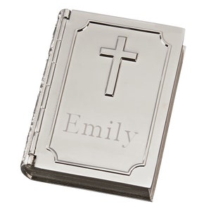 May include: A silver-coloured, book-shaped keepsake box with a cross design on the cover. The name "Emily" is engraved below the cross. The box is closed and has a hinged spine.