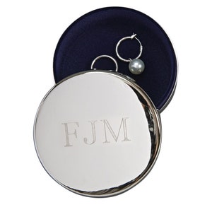 May include: A silver round jewelry box with a blue velvet interior. The box is engraved with the initials "FJM".