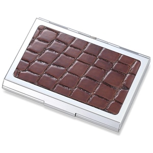 May include: A brown leather card holder with a crocodile pattern, encased in a silver metal frame.