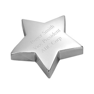 May include: A polished silver star-shaped award with beveled edges. The surface is engraved with the text "Roger Smith, Vice President, ABC Corp." The star is set against a white background, highlighting its reflective surface.