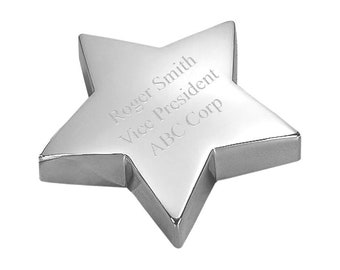 May include: A polished silver star-shaped award with beveled edges. The surface is engraved with the text "Roger Smith, Vice President, ABC Corp." The star is set against a white background, highlighting its reflective surface.