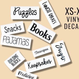 May include: A set of black vinyl decals with various labels for home organization, including "Puzzles", "Snacks", "Books", "Pajamas", "Building Blocks", "Lunch Boxes", "Sugar", "Shampoo", "Keepsakes", and "Medicine".