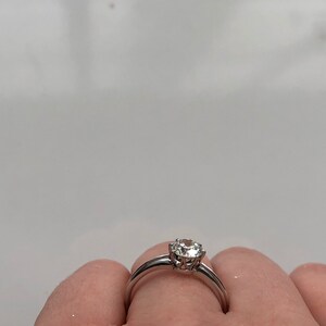 May include: A silver ring with a single round diamond set in a prong setting.