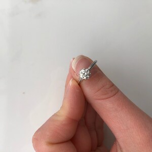 May include: A silver engagement ring with a round, clear diamond.