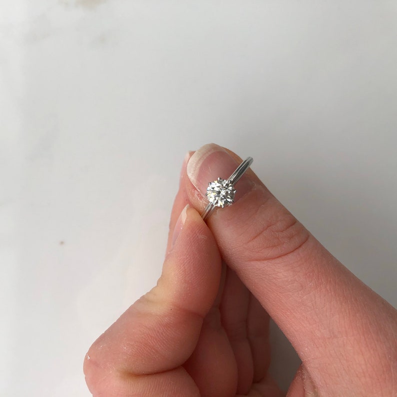 May include: A silver engagement ring with a round, clear diamond.