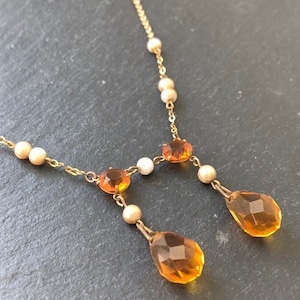 May include: A gold chain necklace with a teardrop-shaped amber pendant. The necklace is adorned with small white pearls.