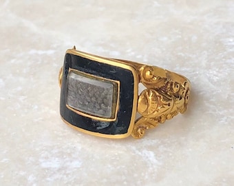 May include: A gold ring with a black enamel rectangular setting and a clear glass stone. The ring has a decorative design on the band.