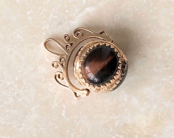 May include: A gold pendant with a brown and black gemstone set in a gold bezel. The pendant is attached to a gold chain with a decorative design.