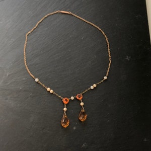 May include: A gold chain necklace with a teardrop-shaped pendant and small orange and white beads.