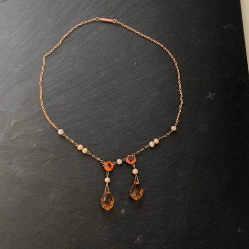 May include: A gold chain necklace with a teardrop-shaped pendant and small orange and white beads.