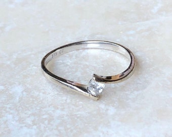 Könnte beinhalten: Ein silberner Ring mit einem einzigen, klaren Stein, der in einem gebogenen Band gefasst ist. Der Ring ist mit "375 CZ" gekennzeichnet.