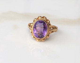 Puede incluir: Un anillo de oro con una amatista ovalada engastada en un diseño floral detallado.