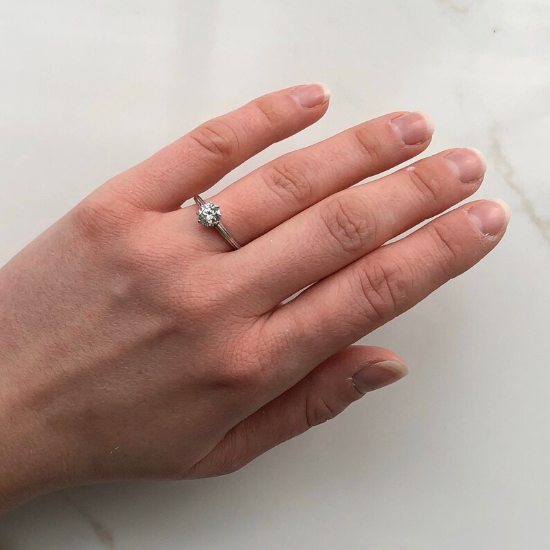 May include: A silver ring with a single round diamond set in a prong setting.