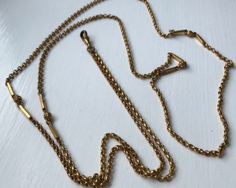 May include: A gold chain necklace with a decorative clasp and three gold bars. The chain is made of two strands of linked circles.