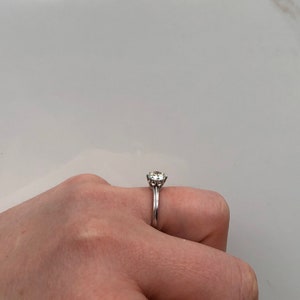 May include: A silver engagement ring with a round, clear center stone and a delicate band.