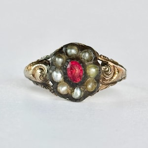 May include: An antique ring with a central oval red gemstone surrounded by small pearls. The ring has a dark setting and ornate gold filigree detailing on the band.