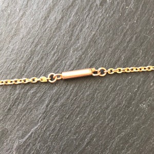 May include: A close-up of a gold chain necklace with a clasp. The clasp is a small, cylindrical tube with a spring-loaded mechanism.