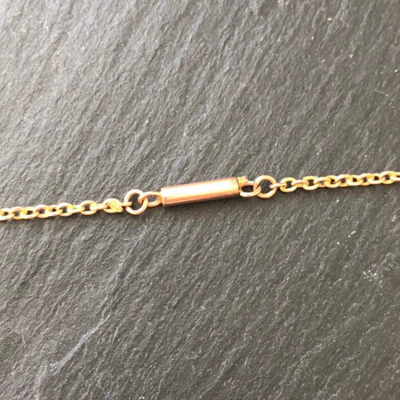 May include: A close-up of a gold chain necklace with a clasp. The clasp is a small, cylindrical tube with a spring-loaded mechanism.