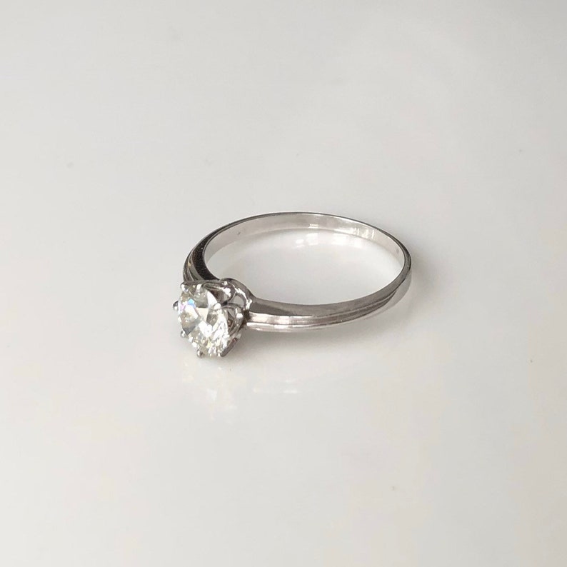 May include: A silver solitaire engagement ring with a round, clear diamond.