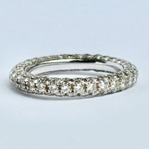 May include: A silver ring with a band fully encrusted with small, round, clear gemstones. The ring is set against a plain white background, highlighting the sparkle of the stones. The ring is a classic piece of jewelry.