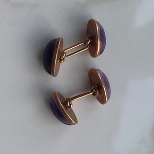 Puede incluir: Un par de gemelos con piedras de vidrio morado engastadas en metal dorado.