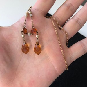 May include: A gold chain necklace with a pendant featuring amber-colored teardrop crystals and small white pearls.