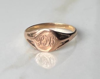 May include: A gold signet ring with a raised oval top featuring the engraved initials "L.H."