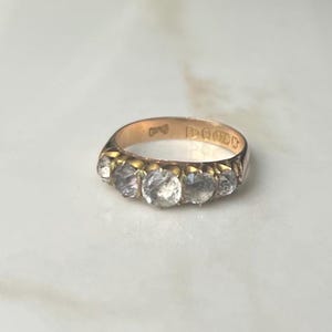 May include: A gold band ring with five clear stones set in a row. The ring is marked "15CT 9CT" on the inside.