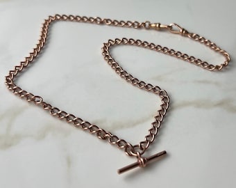 Könnte beinhalten: Eine Taschenuhrkette aus Roségold mit einem T-Bar-Verschluss. Die Kette besteht aus einem filigranen, verlinkten Design.
