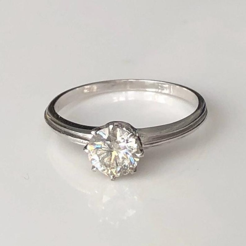 May include: A silver ring with a single, round, clear diamond in the center.
