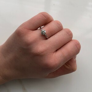 May include: A silver engagement ring with a single round diamond set in a simple band.