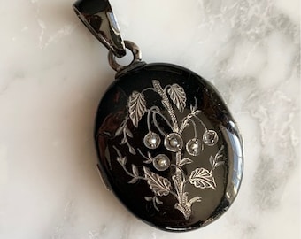 May include: Black oval locket with a silver floral design and pearl accents. The locket has a bail for hanging on a chain.