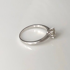 May include: A simple silver band ring with a single, round, clear gemstone set in a four-prong setting.